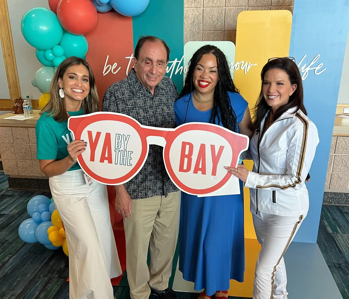 Sorboni Banerjee, R.L. Stine, Tiffany D. Jackson and Linda Bond holding the YA By The Bay glasses sign in front of the festival backdrop