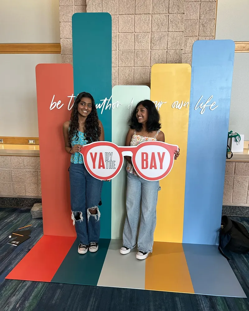 Two students posing with the YA By The Bay sunglasses sign