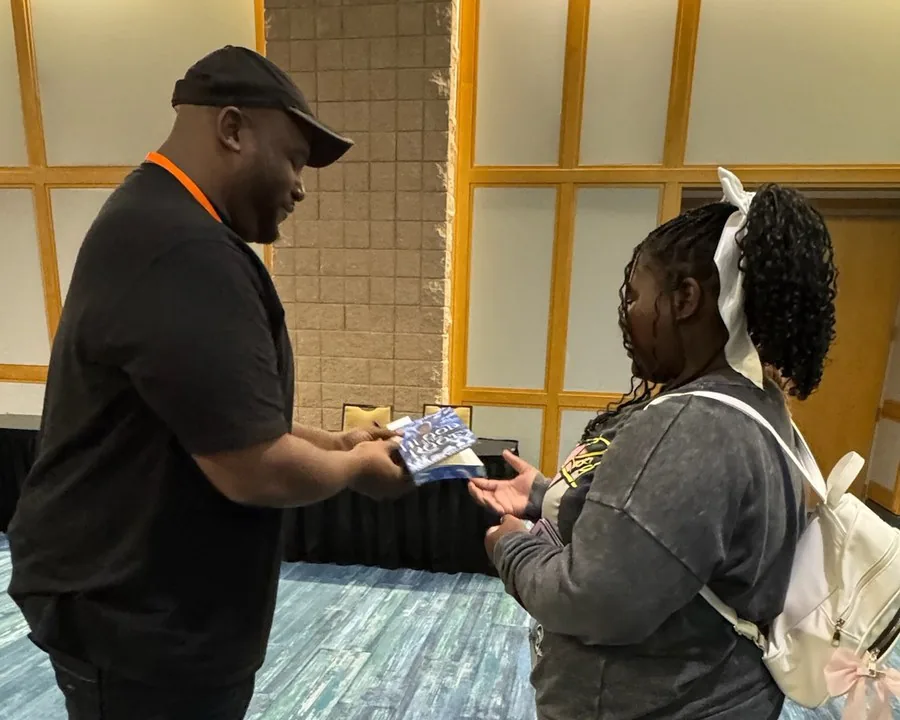 Author LaDarrion Williams handing a student a book