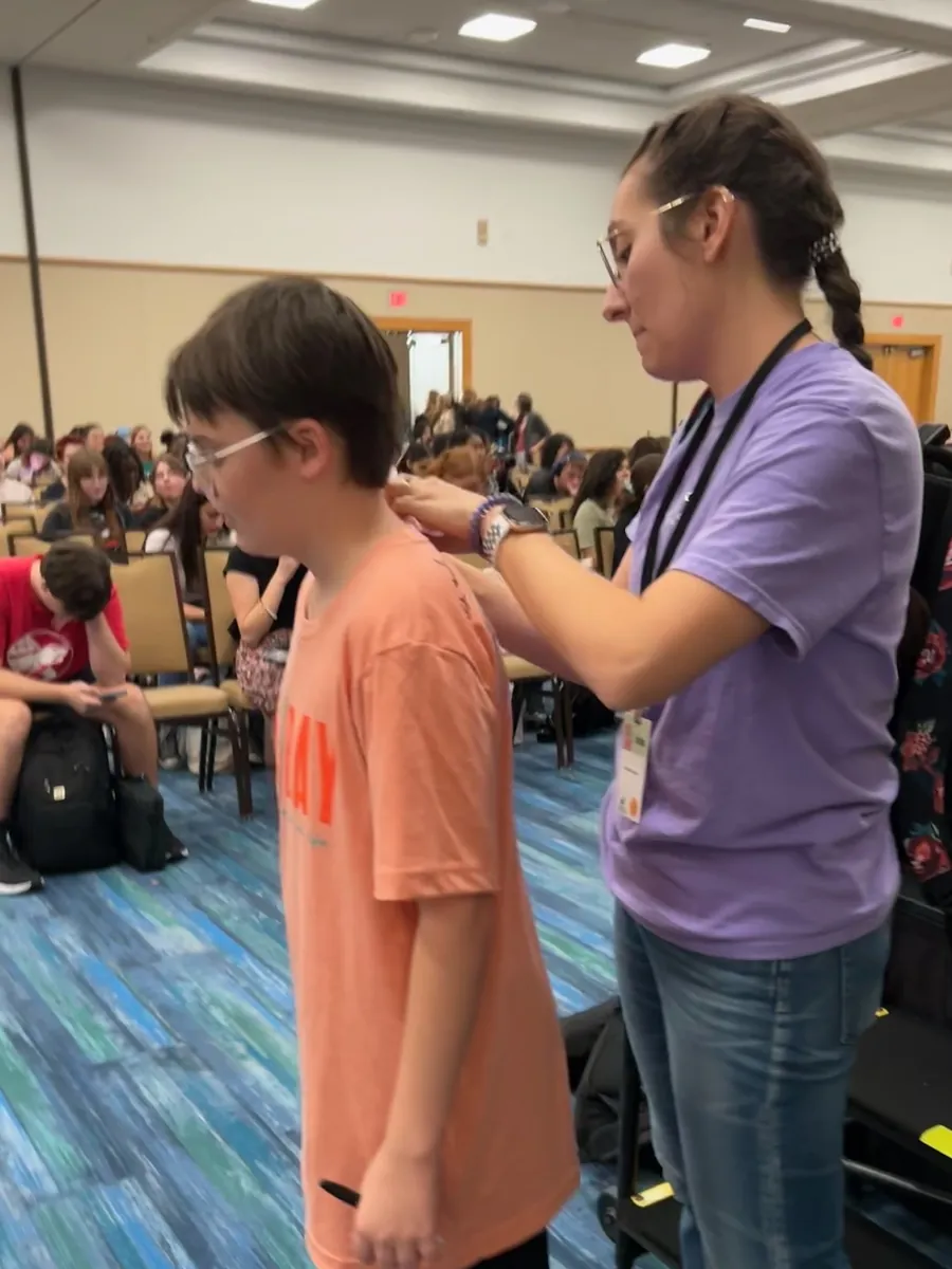 A volunteer fastening a student's festival lanyard beside the stage